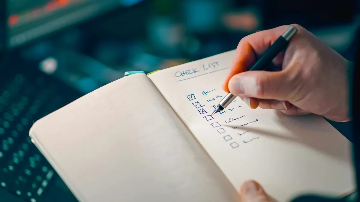 Mão escrevendo em caderno com checklist de planejamento de negócios