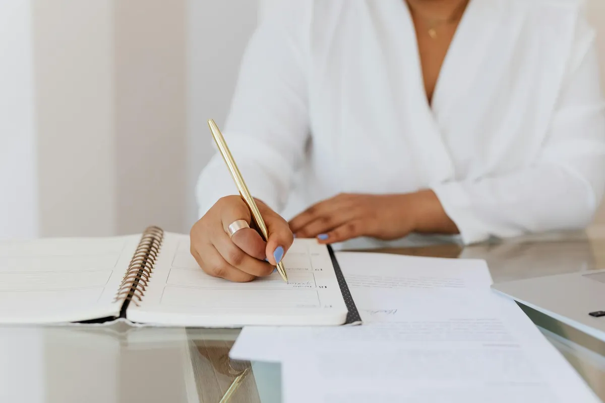 Pessoa escrevendo em caderno com expressão concentrada em ambiente de escritório