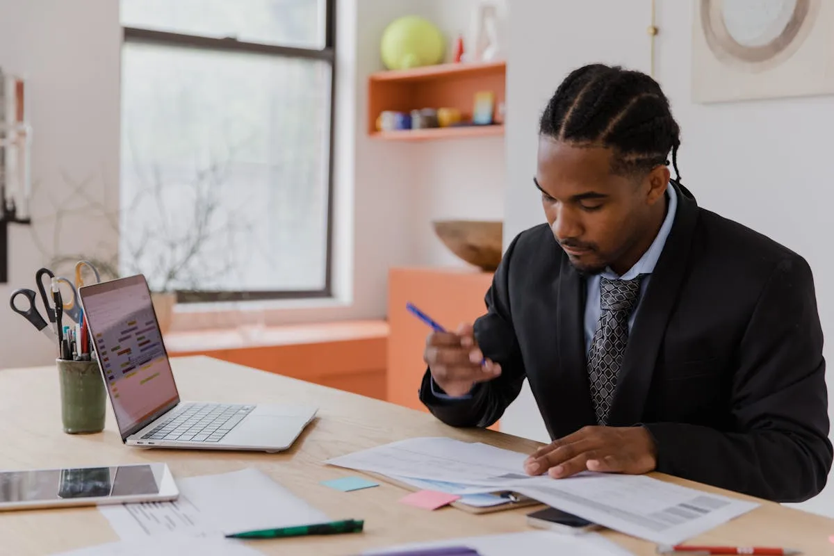 Empresário sentado à mesa com caderno aberto e notebook, organizando informações do negócio