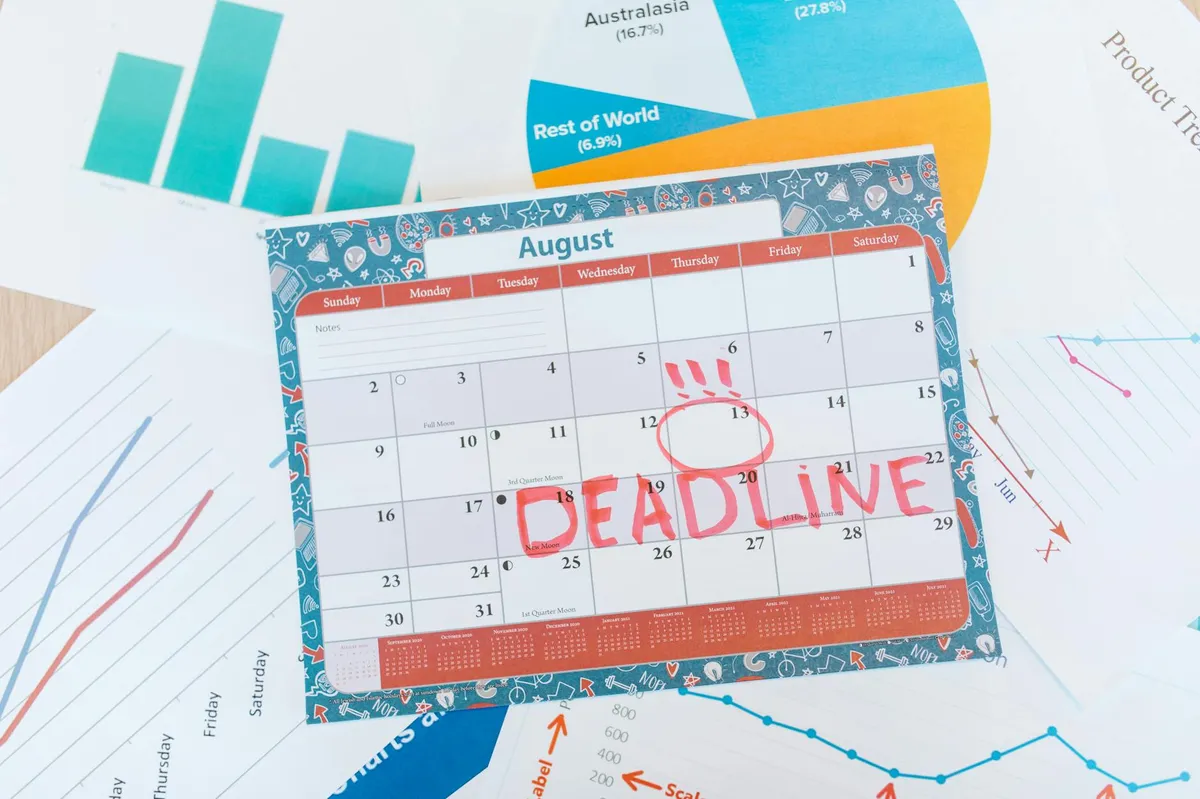 Calendário sobre mesa de trabalho com marcações de prazo e laptop ao lado representando planejamento
