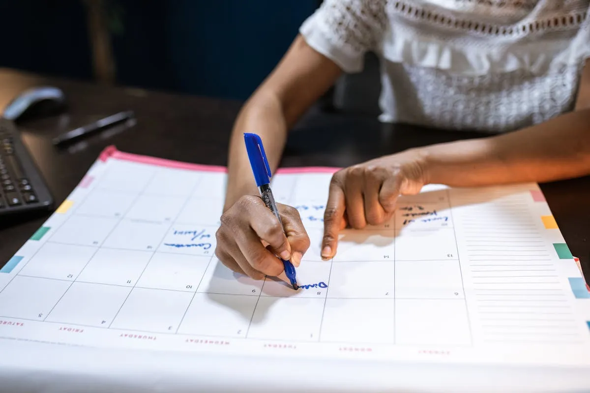 Pessoa apontando para um calendário em uma mesa de trabalho com computador ao fundo