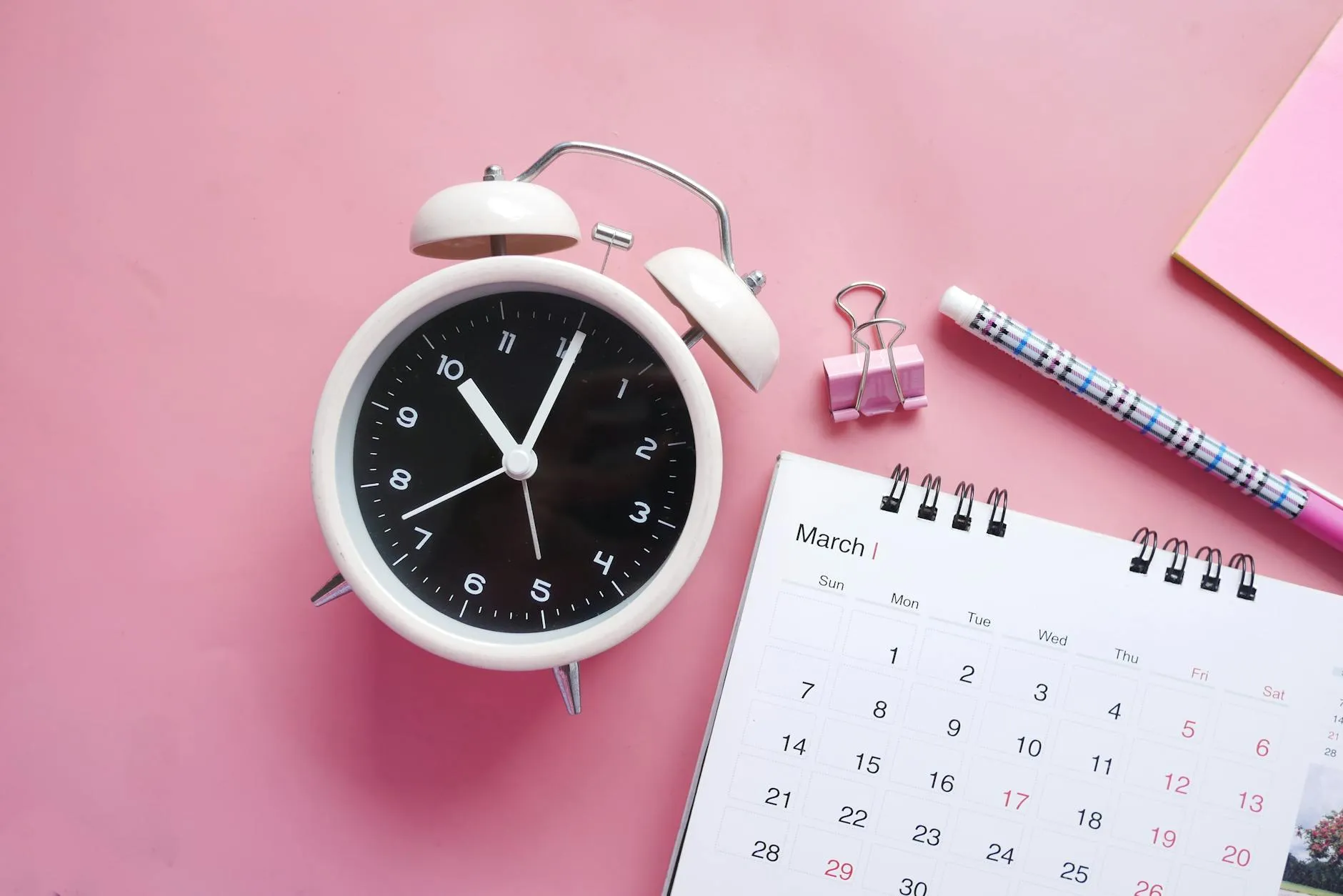 Relógio sobre mesa com agenda de trabalho ao fundo