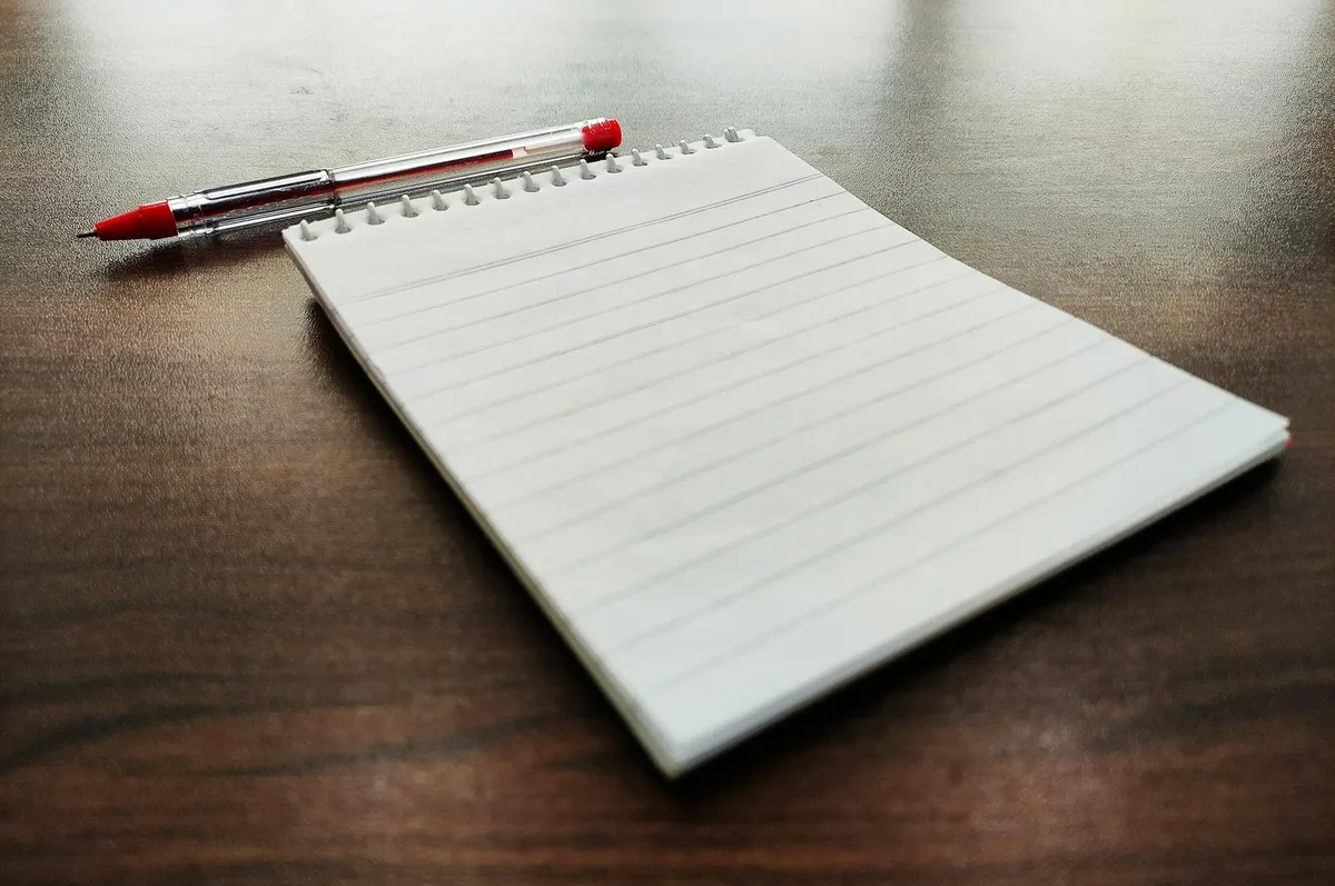 Mão escrevendo em caderno branco sobre mesa de trabalho organizada