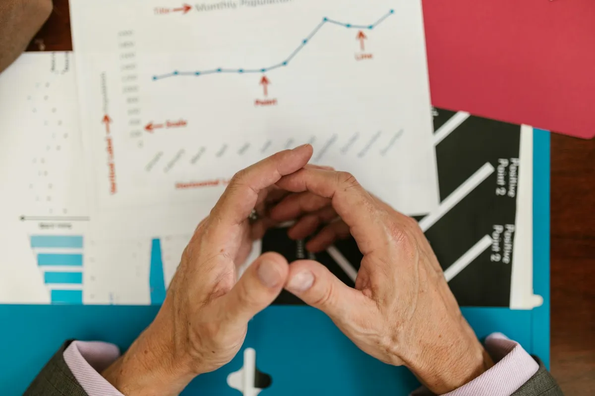 Mãos analisando gráficos e planilhas financeiras em mesa de trabalho de empresa