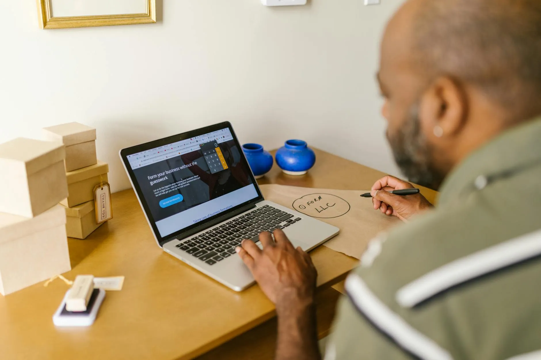 Empresário sentado à mesa com notebook aberto, comparando opções em tela de computador