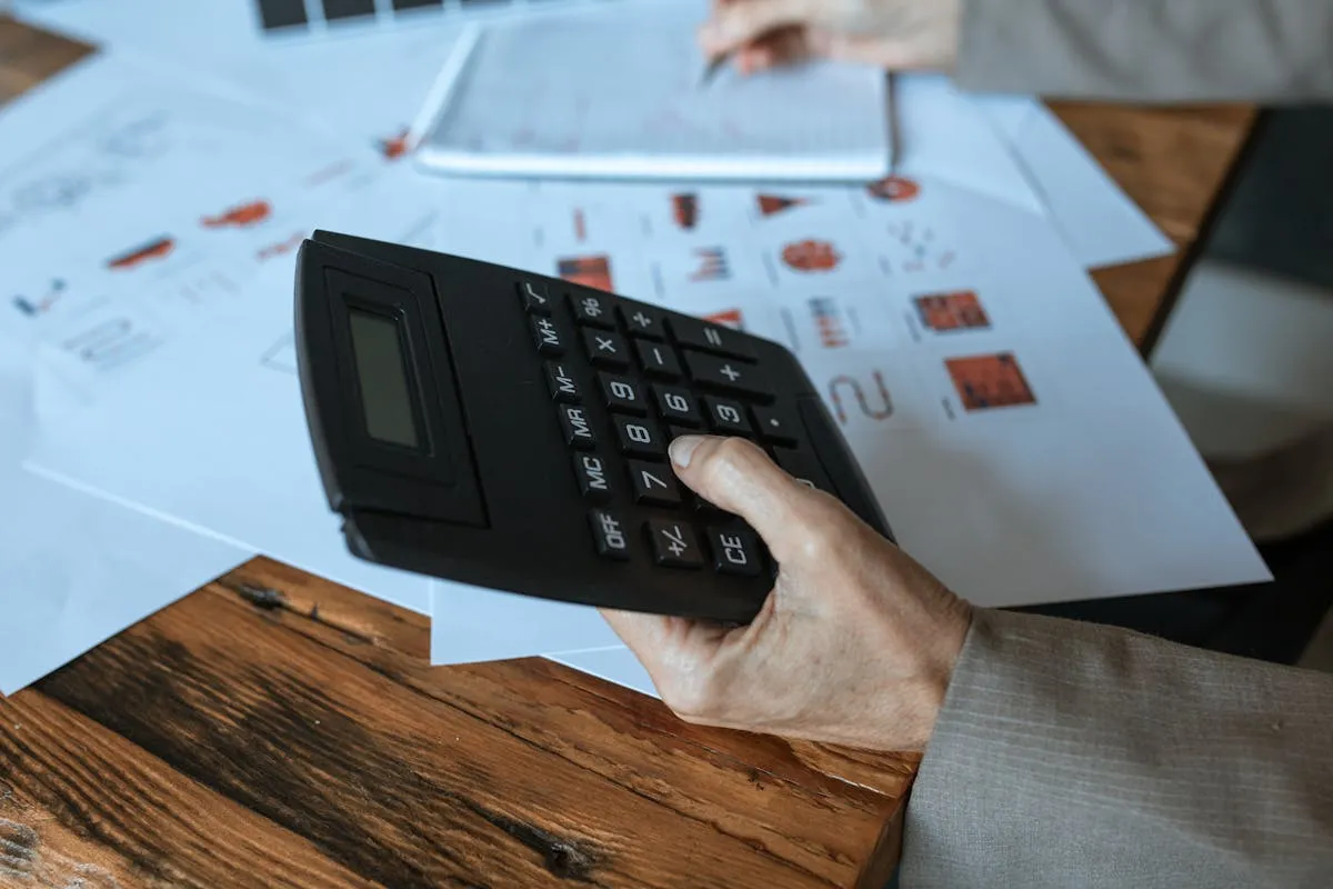 Dono de pequena empresa fazendo contas em uma calculadora com papéis na mesa