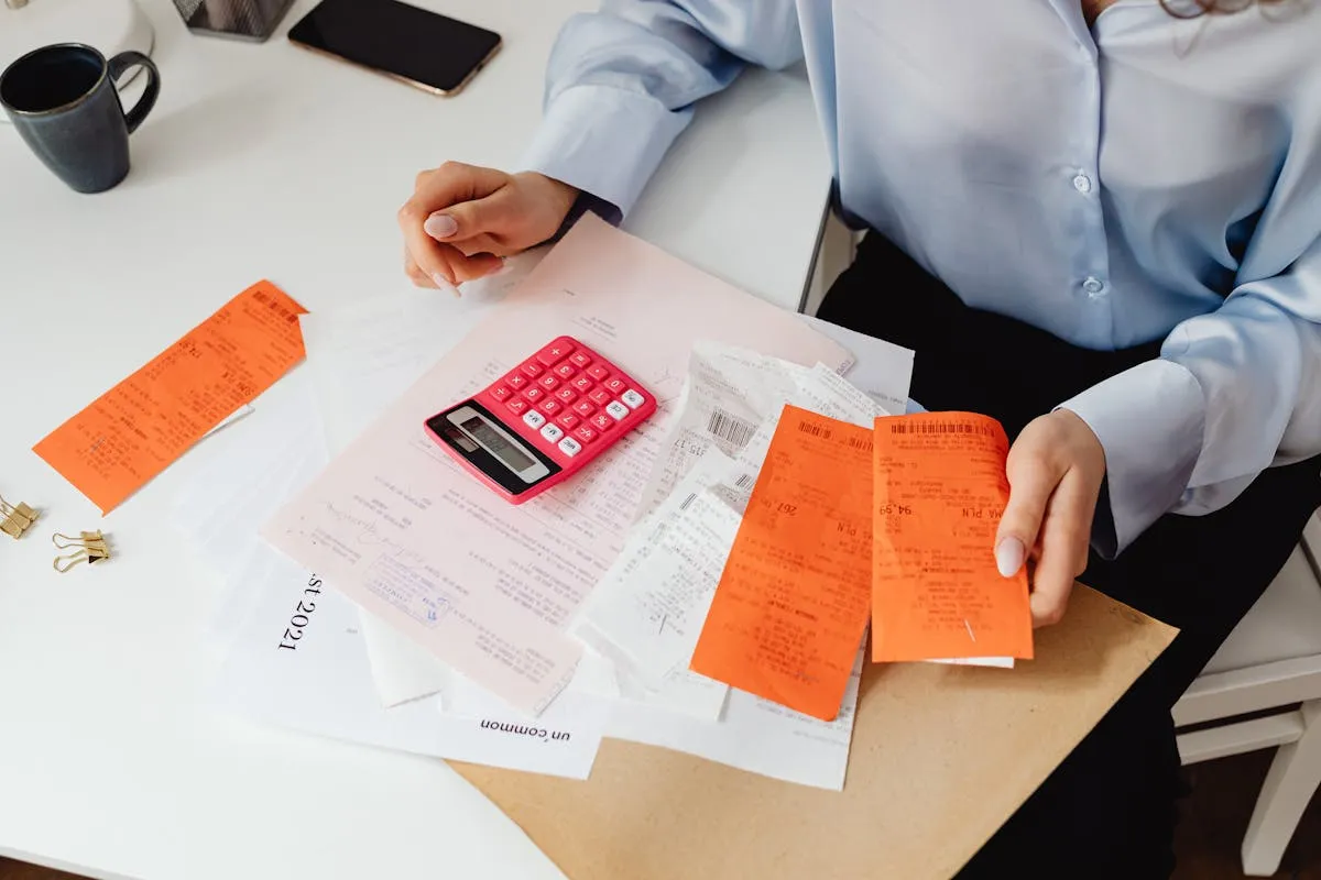 Calculadora e notas fiscais em mesa de escritório com notebook ao fundo
