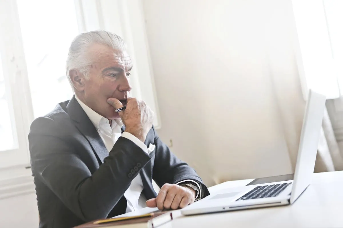 Dono de negócio pensativo olhando para notebook com gráficos financeiros na tela